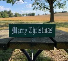 a merry christmas sign sitting on top of a wooden bench in front of a field