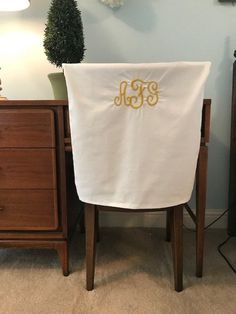 a chair with a monogrammed table cloth on it in front of a dresser