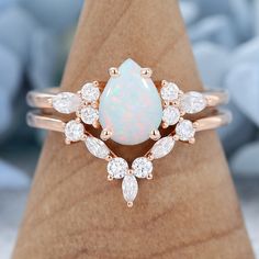 a white opal and diamond ring sitting on top of a wooden stand