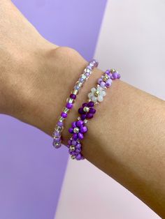 a woman's arm wearing two bracelets with purple and white beads on it