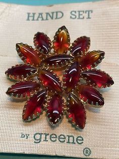 a red and yellow broochle sitting on top of a white cloth covered box