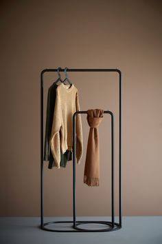 two sweaters hanging on clothes racks in front of a brown wall and tan background