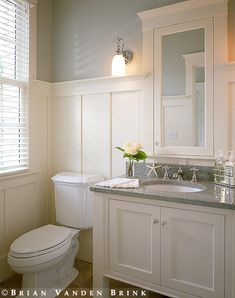 a white toilet sitting next to a sink in a bathroom under a window with shutters