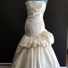 a white wedding dress on display in front of a black wall with a blue top