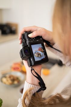 a woman holding up a camera to take a photo with food on the table behind her