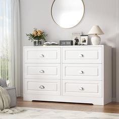 a white dresser with drawers and a round mirror on the wall above it in a bedroom