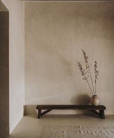 a wooden bench sitting in front of a wall with a vase on top of it