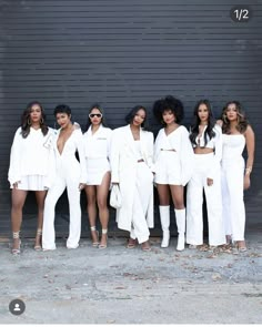 a group of women standing next to each other in front of a garage door wearing white outfits