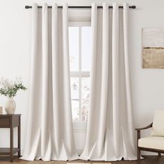 a white curtain hanging in front of a window next to a wooden table and chair