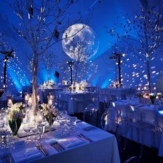 a room filled with lots of tables covered in white linens and decorated with trees