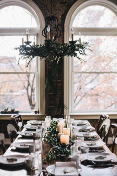 a long table set with place settings and candles in front of two large windowed windows