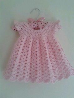 a pink crocheted baby dress hanging on a wall with a bow at the neck