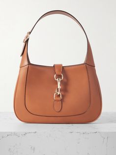 Gucci's small 'Jackie' bag takes its curved silhouette from the original style that debuted in the '60s and even boasts the same gold-tone piston clasp. Crafted in Italy from brown leather, it's suspended on a thick strap that can be adjusted to your perfect drop. It has plenty of space inside for everyday essentials, like your wallet, keys, cell and compact. Gucci Shoulder Bag With Brass Hardware For Evening, Gucci Evening Bag With Brass Hardware, Gucci Bags With Metal Hardware For Work, Gucci Brown Shoulder Bag With Brass Hardware, Classic Gucci Bags With Gold-tone Hardware, Everyday Gucci Shoulder Bag With Gold-tone Hardware, Brown Gucci Shoulder Bag With Brass Hardware, Gucci Cognac Bag For Everyday Use, Everyday Gucci Cognac Bag