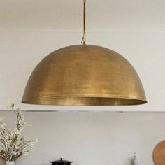 a large brass dome light hanging over a kitchen counter top next to a potted plant