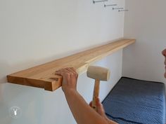 a person holding a hammer up to a wooden shelf on the wall above a bed