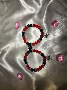 two bracelets with red, black and silver beads on a white satin surface next to pink crystal stones