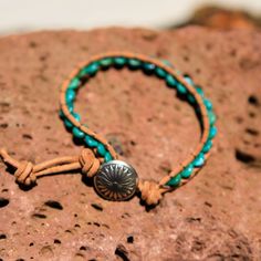 Created by the artists at Alta Studios this Turquoise Bead and Leather Wrap bracelet is hand crafted high in the mountains of Northern New Mexico. Made from genuine high quality turquoise rondelle beads, tan Greek leather cord and cast metal "Concho" button. A beautiful piece of the Southwest! This item is one of a kind - you will receive the exact item pictured. Adjustable length : Approx. 7 3/8" to 8" dia. 12 oz. Shipping Weight Handmade Turquoise Leather Bracelet Spiritual, Adjustable Southwestern Hand Wrapped Jewelry, Southwestern Adjustable Hand Wrapped Jewelry, Southwestern Hand Wrapped Adjustable Jewelry, Adjustable Southwestern Style Hand Wrapped Jewelry, Adjustable Turquoise Leather Bracelet In Rustic Style, Adjustable Beaded Turquoise Leather Bracelet, Adjustable Turquoise Beaded Leather Bracelet, Rustic Adjustable Turquoise Beaded Bracelets