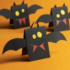 some black paper bats with yellow eyes and red noses are on an orange tablecloth