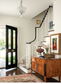 an entryway with a wooden table and black doors, white railings and framed pictures on the wall