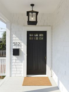 a black front door on a white house with a light hanging from it's side