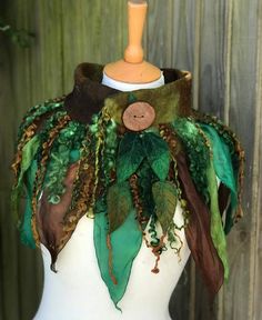 a white mannequin wearing a green and brown scarf with leaves on it's back