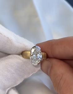 a person holding a diamond ring on top of a white cloth covered napkin with a gold band