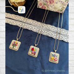 three necklaces with flowers on them are hanging next to a box and lace doily