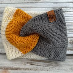 a knitted headband with an orange and grey knot on it, sitting on top of a wooden surface