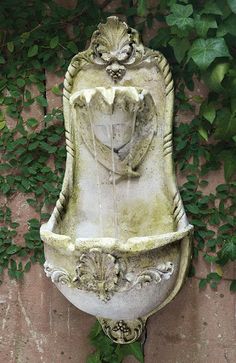 a water fountain in front of a brick wall with ivy growing on it and vines around it