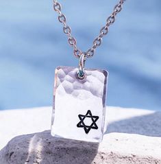 This necklace is sure to become a valued part of your own Judaica jewelry collection because of its unique combination of current elegance and traditional faith. Any friend of Israel and the symbols represented by this star would like to receive this necklace as a holiday gift! ➤FEATURES Pendant - 7/8'' x 5/8'' Choose chain ➤CHOOSE CHAIN 1. Dark metal - rolo chain - 2.4mm 2. Ball chain stainless steel - 2.4mm 3. Regular stainless steel chain - larger links  4. Regular stainless steel chain - smaller links 5. Ball chain - dainty ➤CHAIN LENGTHS Ball chains are 24 inches and can be shortened by snipping with scissors. Regular chains are 20 inches and can be ordered in other lengths.  Dark rolo chain is 20 inches ➤CRAFTSMANSHIP Everything Beautiful designs jewelry using only the highest qualit Symbolic Stamped Necklace For Gift, Symbolic Stamped Necklace For A Gift, Symbolic Hammered Necklaces As Gift, Symbolic Hammered Necklace As Gift, Engraved Sterling Silver Star Of David Necklace, Symbolic Hammered Necklace For Gift, Symbolic Necklace For Father's Day Gift, Spiritual Engraved Necklace For Father's Day, Symbolic Dog Tag Necklace As Gift