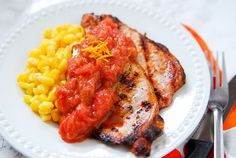 grilled chicken, corn and tomato sauce on a white plate with utensils