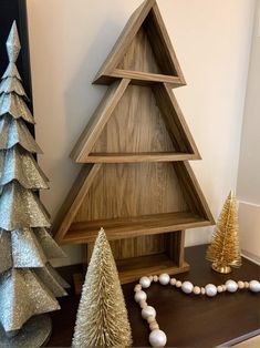 three wooden christmas trees on a table next to other ornaments and decorating items in gold, silver and white