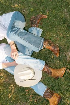 two people sitting in the grass with cowboy boots and hats on their feet, one wearing a white shirt