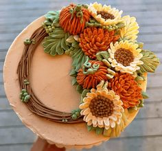 a cake decorated with sunflowers and leaves on top of a wooden table next to a brick wall