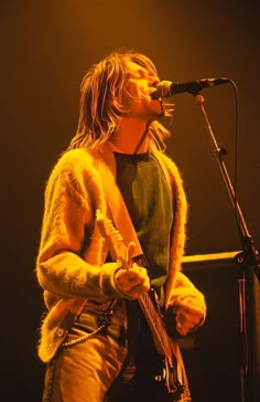 a man that is standing up with a guitar in front of him and singing into a microphone