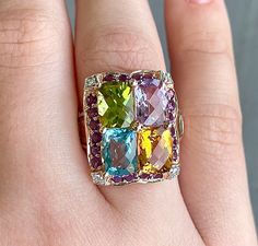 A multicolored gemstone ring, that is VERY. HEAVY on the gemstones, 14k Rose Gold, currently a size 5 1/4. The Gemstones are Blue Topaz, Citrine, Peridot, and Amethyst. There are 2 more citrine, and 2 blue topaz on the sides of the band. There is a darker purple amethyst halo around the large stones with 4 small diamond accents in the corners with white gold prongs on the small diamonds. 1x 6.0x7.5mm cushion cut light amethyst 1x 6.0x7.5mm cushion cut citrine 1x 6.0x7.5mm cushion cut blue topaz 1x 6.0x7.5mm cushion cut peridot 2x 5.0x2.9mm tapered rectangle citrine 2x 4.2x2.4mm tapered rectangle blue topaz 4x 1.2mm round diamonds 20x 1.6 round dark amethyst Luxury Multicolor Multi-stone Gemstones, Formal Multicolor Fine Jewelry Gemstones, Multicolor Diamond Gemstones With Accents, Luxury Multicolor 14k Gold Gemstones, Luxury Multicolor Gemstones With Accents, Luxury Multicolor Gemstones, Luxury Multicolor Rings With Gemstone Accents, Fine Jewelry Multicolor Oval Gemstones, Oval Multicolor Diamond Gemstones