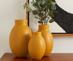 three yellow vases sitting on top of a wooden table next to a framed painting