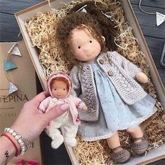 a hand holding a doll in a box with other dolls and decorations on the table