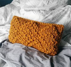 an orange knitted pillow sitting on top of a bed