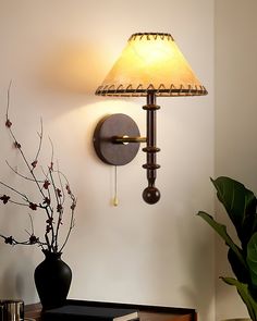 a lamp that is on the wall next to a vase with some flowers in it