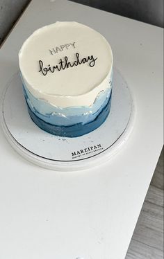 a white and blue birthday cake sitting on top of a table