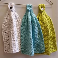 three knitted scarves hanging from a clothes line on a hanger in front of a white wall