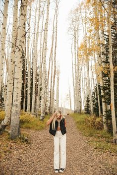 a woman standing in the middle of a forest with her hands on her head and looking up