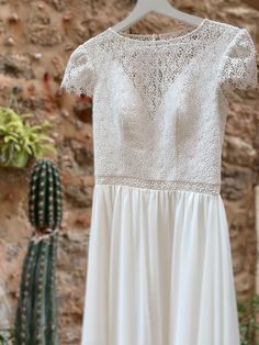 a white dress hanging on a brick wall next to a cactus