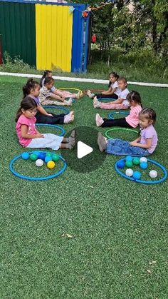 several children are sitting on the grass playing with their toy balls and hula hoop