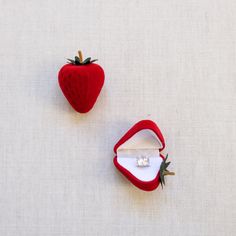 two small red strawberry shaped objects sitting on top of a white cloth covered table next to each other