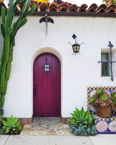 a red door sits in front of a white stucco house with potted plants on either side