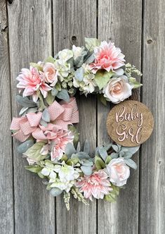 a baby girl wreath with pink flowers and greenery hanging on a wooden fence next to a sign that says baby girl