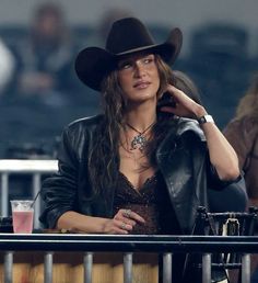 a woman with long hair wearing a cowboy hat and leather jacket at a baseball game