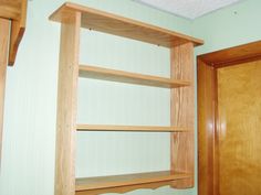 an empty wooden shelf in the corner of a room with green walls and wood trim